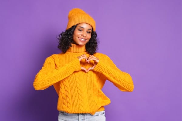 Woman in sweater making heart gesture from hands